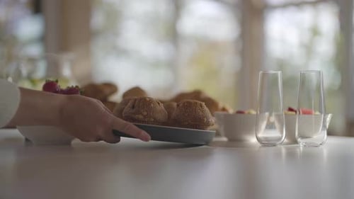 Die Hand einer Frau legt einen Teller mit Muffins auf eine Küchentheke mit anderen Frühstücksspeisen in der Bar