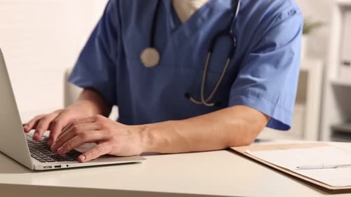 Medical worker working on laptop at table in clinic, closeup