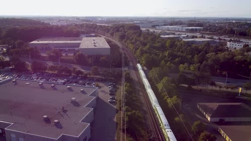 Drone shot following train at a steady speed, an Industrial area with an almost full parking lot. Cr