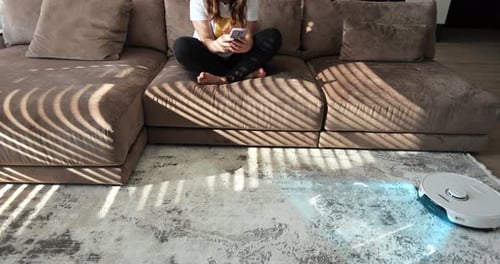 Woman Using Phone While Robot Vacuum Cleans Rug