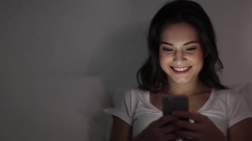 Smiling Woman Using Mobile Phone in Bed at Night