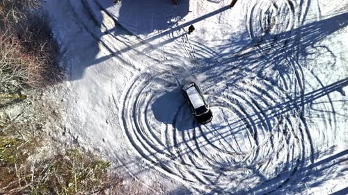 Aerial top-down view of a car drifting in tight circles on a snowy frozen surface, leaving bold