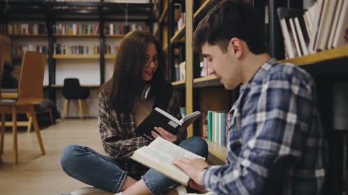 Students Engaged in Reading and Studying Together in a Library Surrounded By Bookshelves on a Quiet