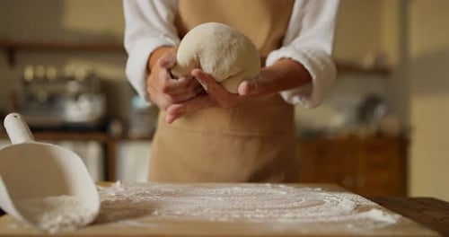 Girl Baker in a White Shirt and Beige Apron Holds Soft Dough in Her Hands and Kneads It While