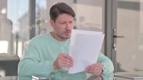 Man Reads and Compares Documents at Glass Table