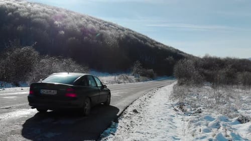 Weitwinkelaufnahme eines Autos, das an einem Wintertag vorbeifährt und verschwindet, trockene Straße und verschneiter Hintergrund
