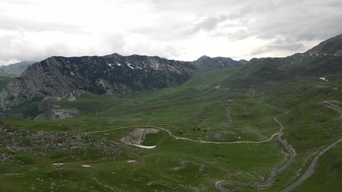 A green valley surrounded by beautiful mountains and a mountain road passing through the valley.