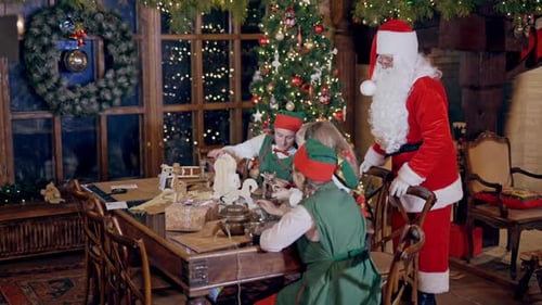 Santa Claus, elves in green costumes and two kids preparing gifts and letters for holiday.