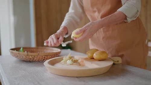 Close-up of mother's hands carefully peeling potatoes on a wooden cutting board in a bamboo kitchen.