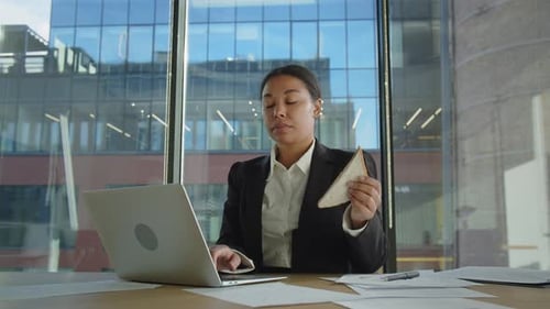 Junge afroamerikanische Frau tippe auf dem PC etwas mit einer Hand und isst mit einer anderen schwarzen Frau in
