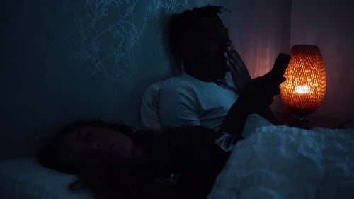 Un homme bâille alors qu'il est assis dans son lit tard dans la nuit sur son téléphone intelligent