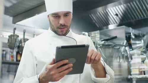Professional chef in a commercial kitchen in a restaurant or hotel is using a tablet computer.
