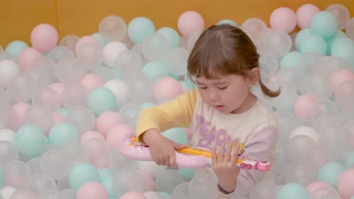 Jolie petite fille jouant sur une guitare jouet dans une fosse à balles colorée au ralenti. Aire de jeux intérieure.
Sac
