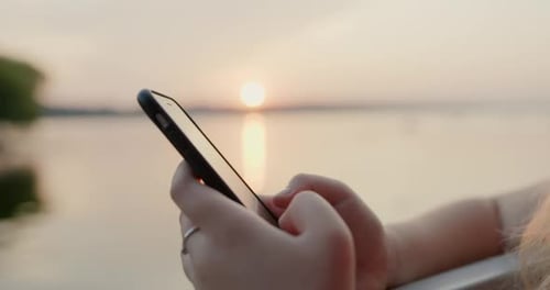 Woman Using Phone at Sunset Over Water