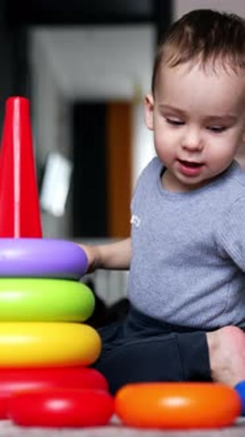 Un niño de un año construye una pirámide de juguete. Bebé jugando en casa. Telón de fondo de sala de estar.