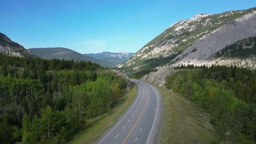 Aerial Drone View of Cars Driving on Winding Paved Road Through Mountain Valley Forest on Sunny Day