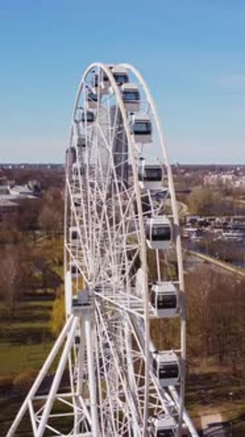 Tall white Ferris wheel spins above Riga city park with skyline in clear spring weather