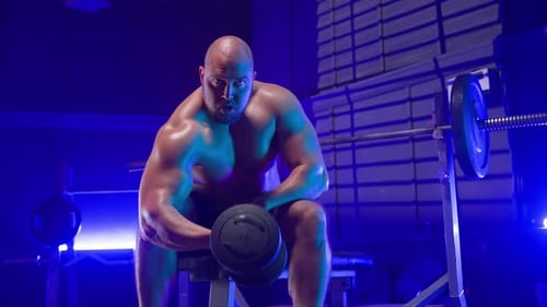Muscular Man Lifting Dumbbell in Gym at Night