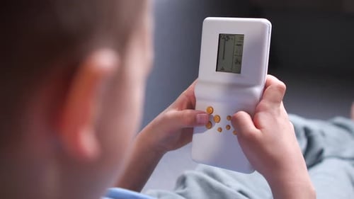 Closeup of a Boy Playing Old Handheld Console Video Game While Sitting on Sofa