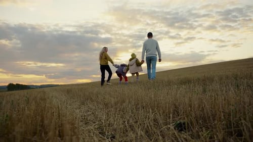 Family Walking Together in Golden Grassy Field at Sunset