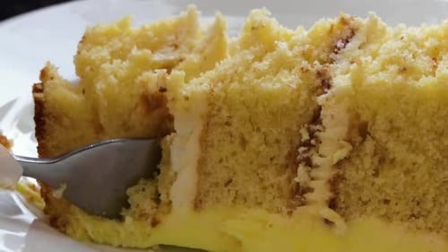 Slice of cake being cut and picked up with a fork. Close up slider shot, on white plate.