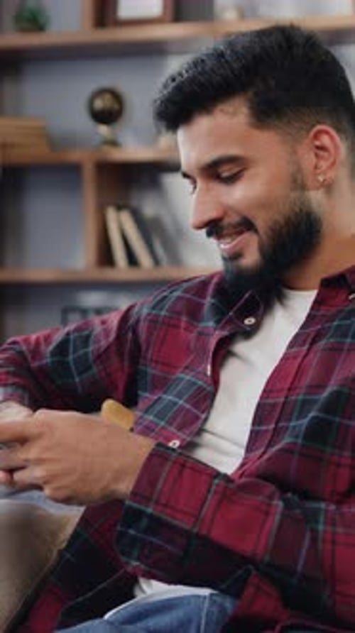 Man Smiling, Uses Mobile Phone on Couch at Home