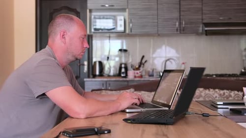 Side view man working on two laptops typing program code on keyboard. IT specialist
