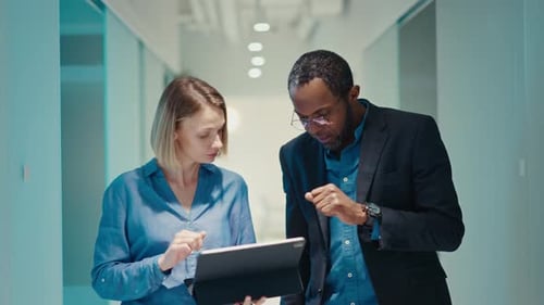 Colleagues Collaborating on a Tablet in a Bright Office Hallway