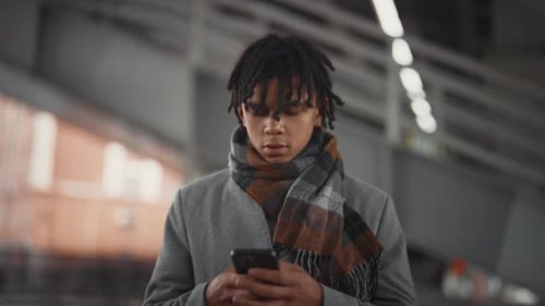 Young African American Man with Dreadlocks Standing Alone on City Street in Fall Mobile Gadget
