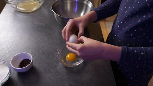 Zoom sur un gros plan d'une jeune fille cassant un œuf dans un bol en verre. Style de vie familial heureux.