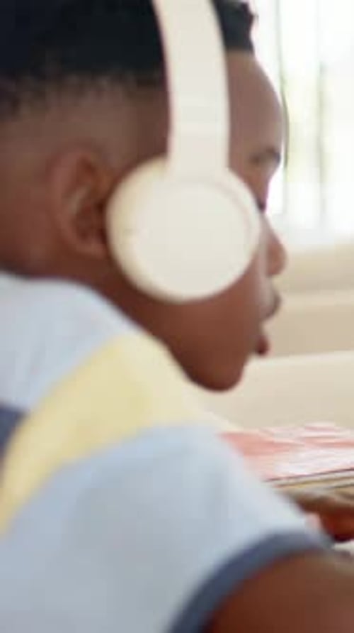 Vertical video: Listening to lesson, boy in striped tee reading at home desk with headset, red book