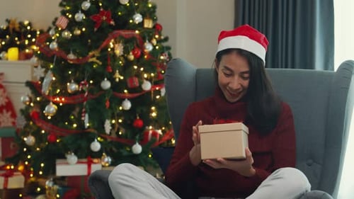 Woman Opening Christmas Gift by Decorated Tree