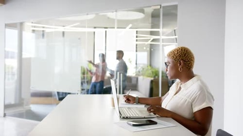 Working in modern office, woman using laptop and writing notes at desk, copy space
