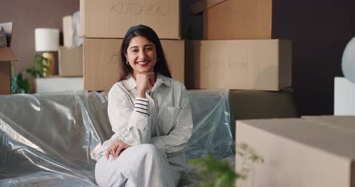 Smiling woman sits amongst moving boxes at home