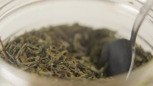 Close-up of spoon taking out a pile of green tea leaves out of a glass jar in 100 FPS. Camera is lo