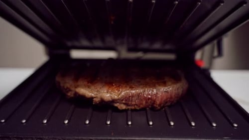 Slow Motion Medium Shot Of Cooked Steak Resting On Open Grill With Steam Rising Showing Finished