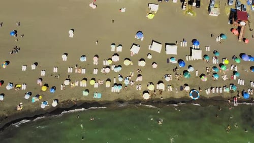 Aerial view of sandy beach with colorful umbrellas, people swimming in sea bay