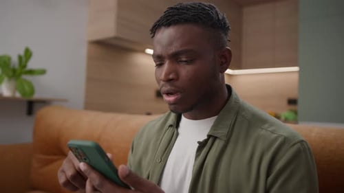 Adult Man On Couch Using Smartphone, Frustrated