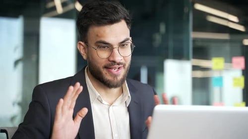 Smiling businessman in a formal suit talking on a video call using a laptop in office. A friendly