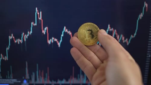Hand Holding Bitcoin Coin in Front of Stock Chart