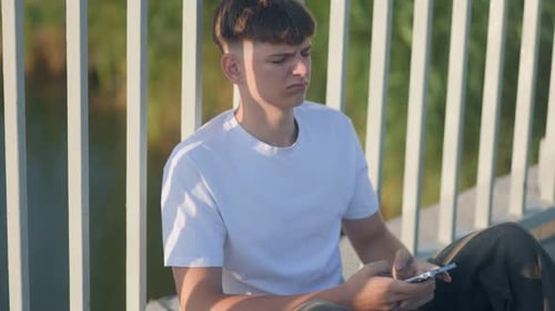 Teenage Boy Sitting Outdoors Using Mobile Phone
