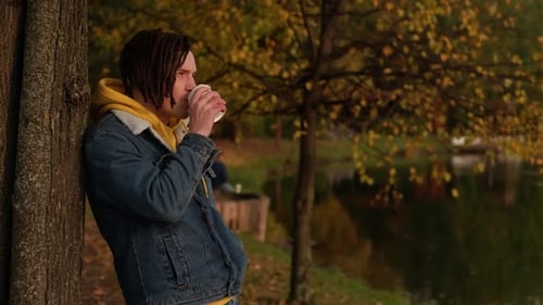 Young Adult Drinking Coffee by Lake in Autumn