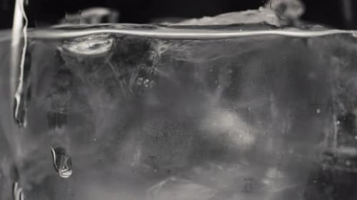 Water and ice swirl together in glass in black and white