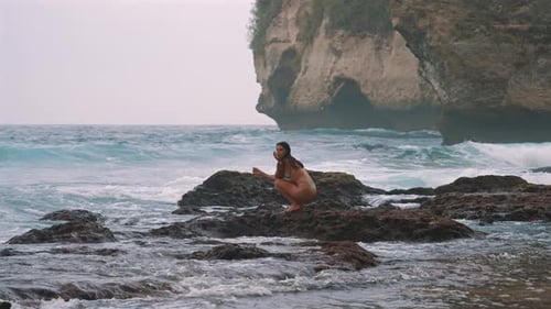Woman Sitting on Rocky Shore with Ocean Waves at Nusa Penida