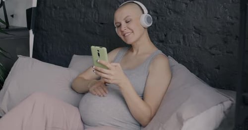 Pregnant Woman Using Phone on Bed with Headphones