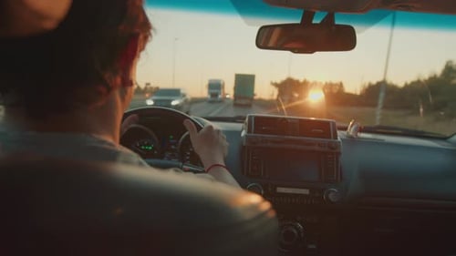 Young Man Steers the Car in Heavy Traffic on the Highway Full of Trucks