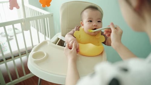 Baby Being Fed With a Spoon in Highchair