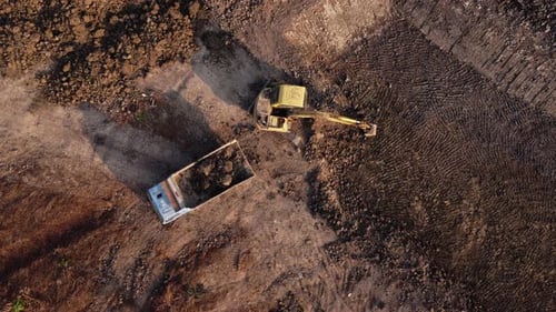 Aerial view of a wheel loader excavator with a backhoe loading sand into a heavy earthmover