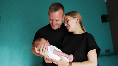 First time parents stand together holding a newborn. Couple looks at their baby with adoration.