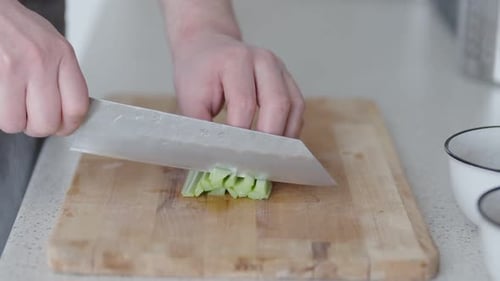 Person, die frische Gurke auf einem Holzbrett fein hackt